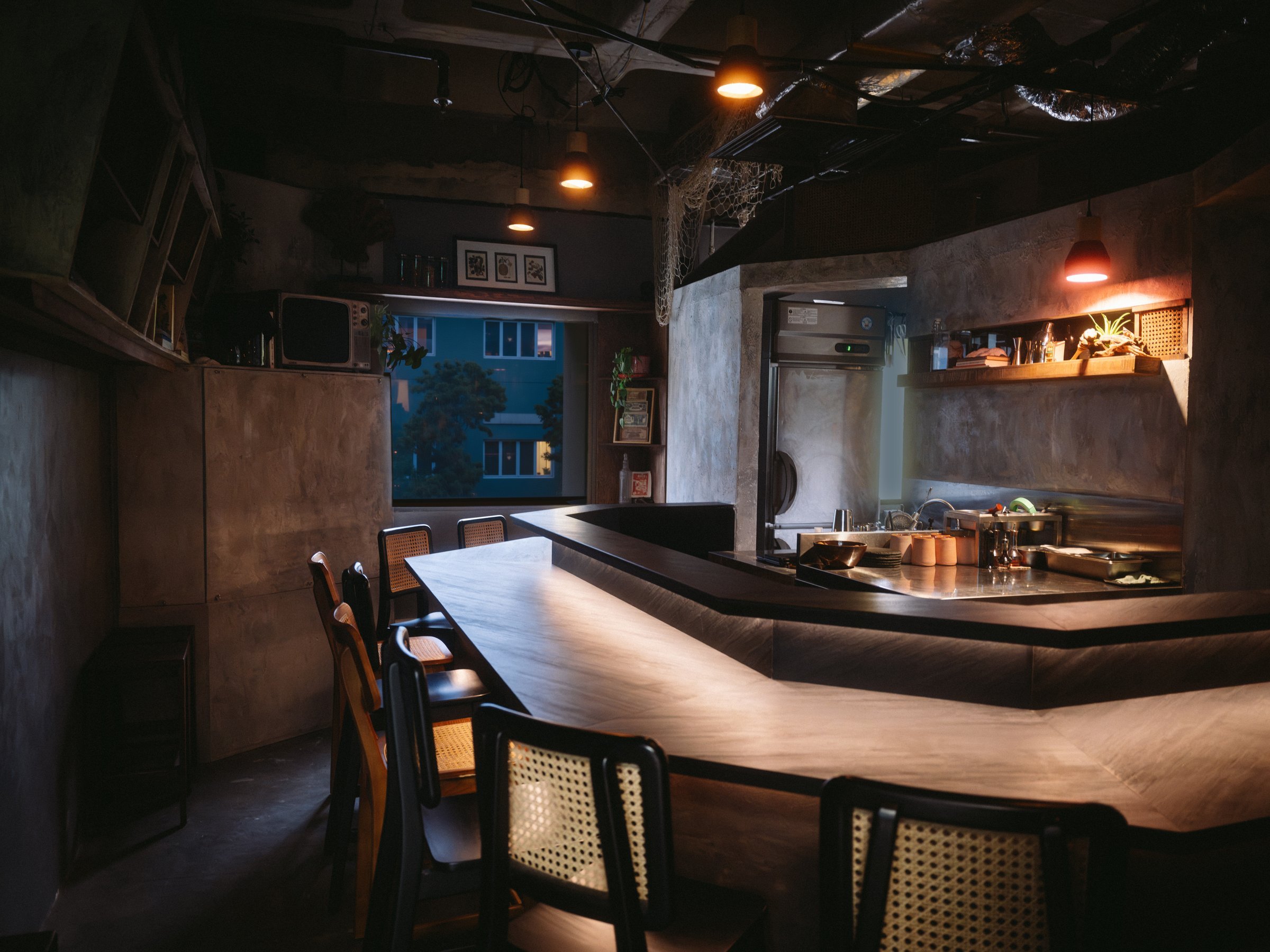 Interior of Laut Singapore, a cocktail bar at Fortune Centre with a marble bar counter, warm pendant lighting, and a dusk view through the window.